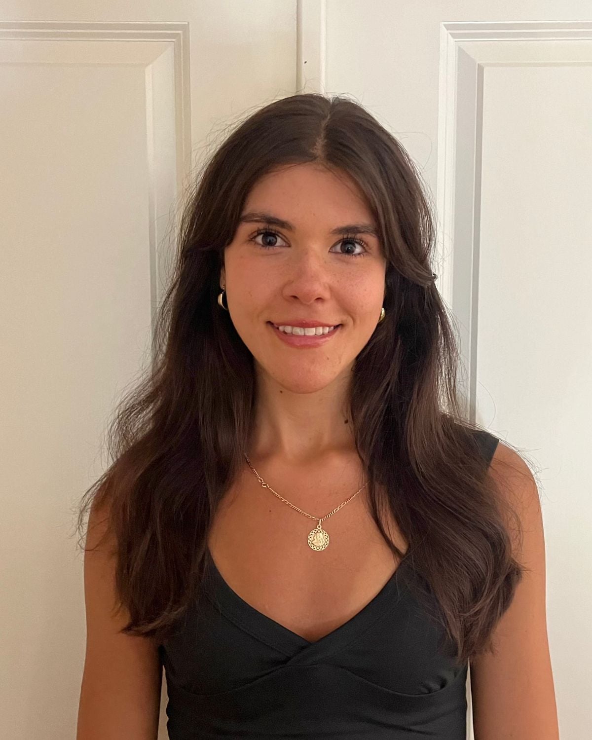 Anteja is wearing a black t-shirt with a gold necklace. She is standing against a white backdrop.