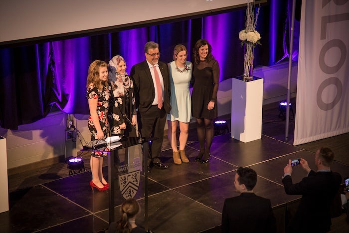 President and Vice-Chancellor Feridun Hamdullahpur stands beside VIP women at 2018 IWD dinner.