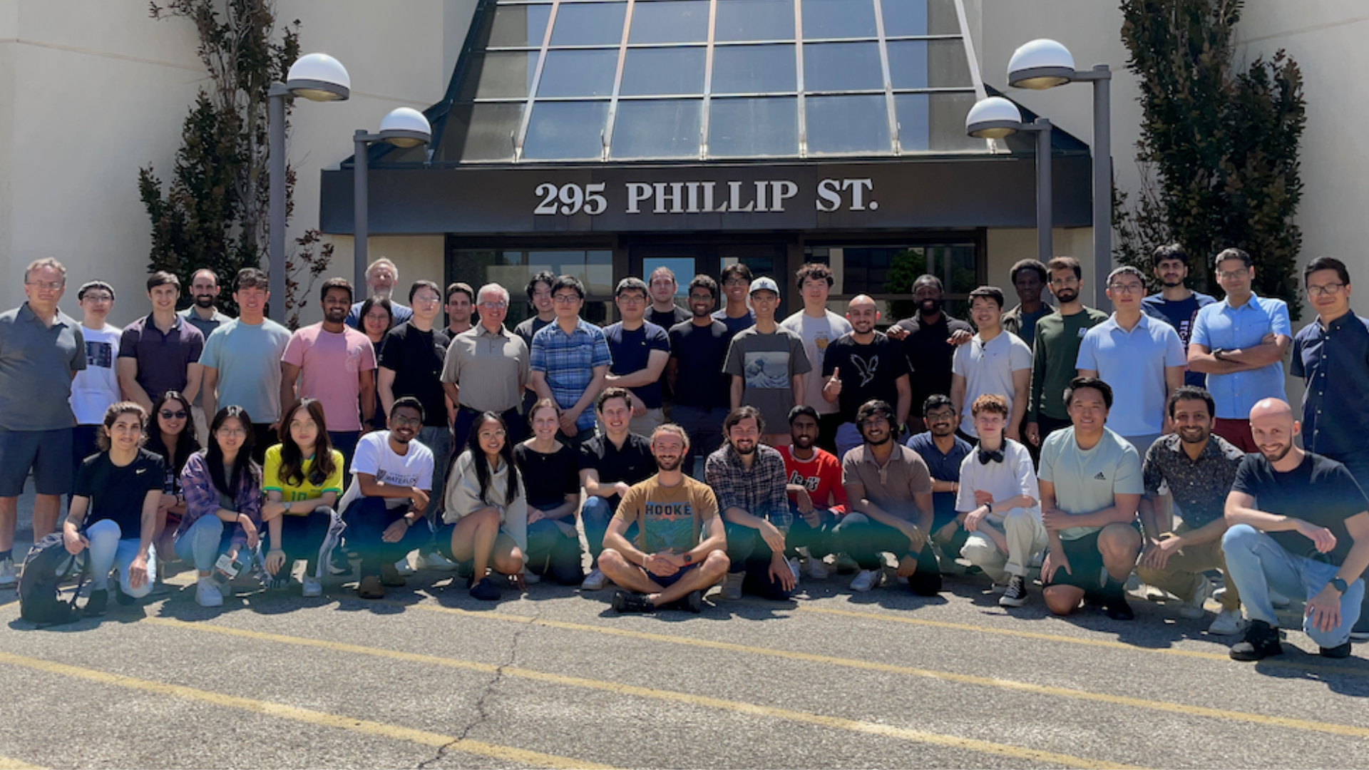 A group of students and faculty members posing in front of a University of Waterloo building