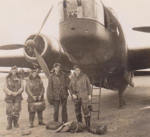 Four young airmen stand under the wing of an airplane
