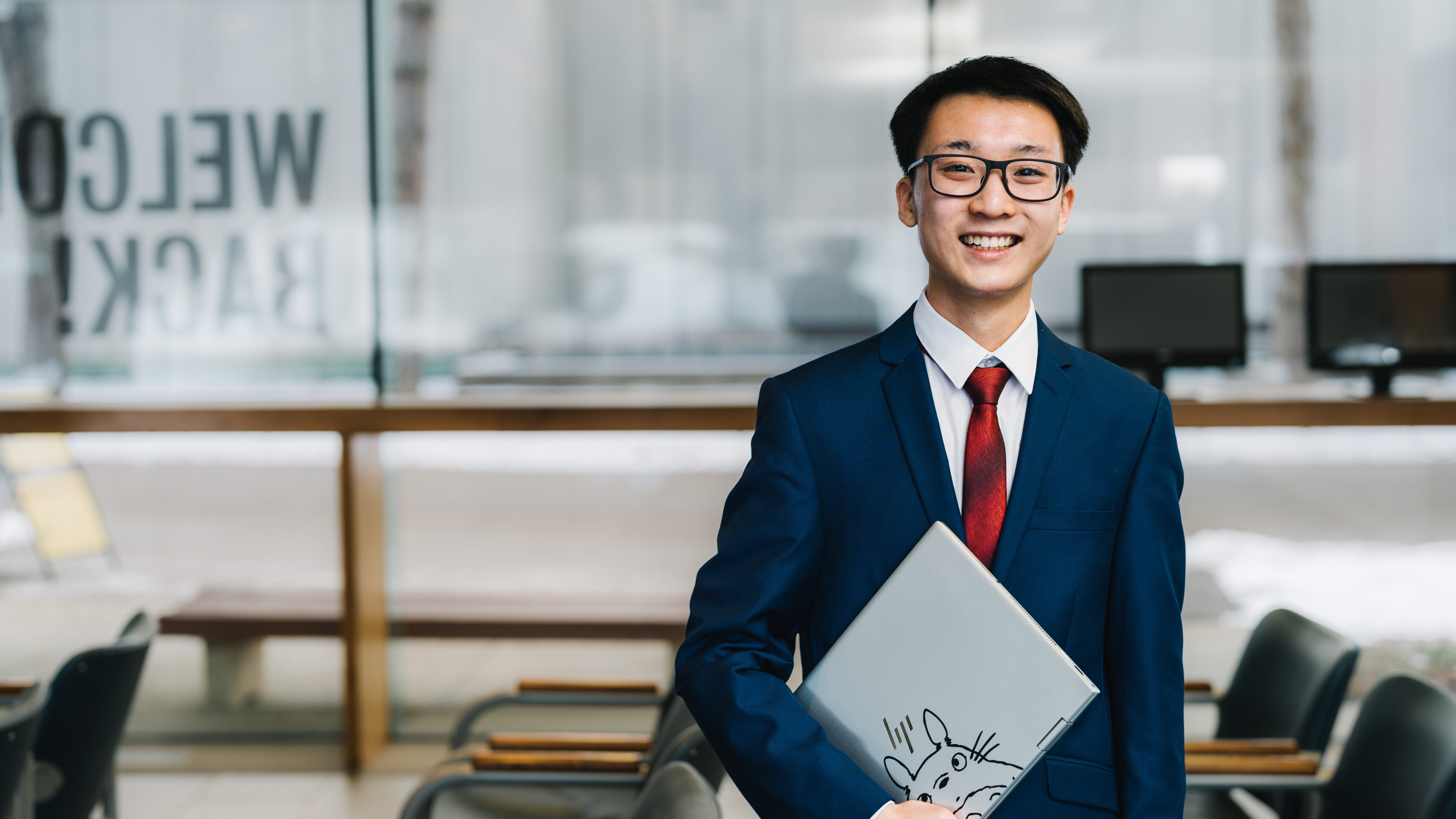 Isaac Cheng wearing a suit and tie and holding a laptop