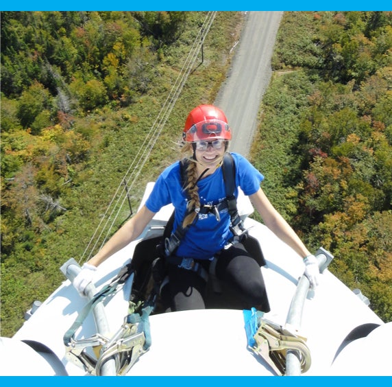 Daniela wearing a red helmet smiling into the camera on the side of a tall white tower.