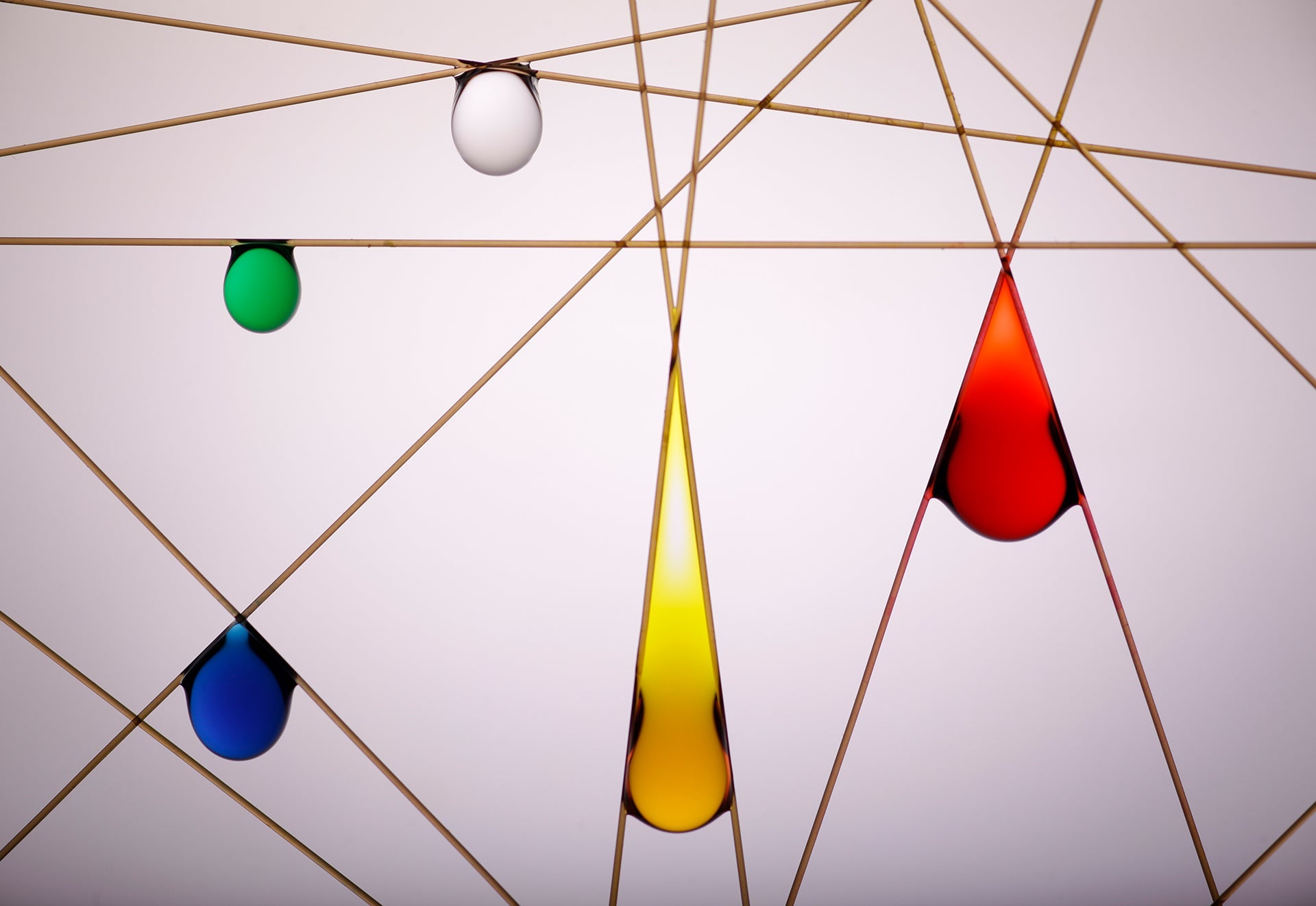 Colured water droplets hang from intersecting fibres.