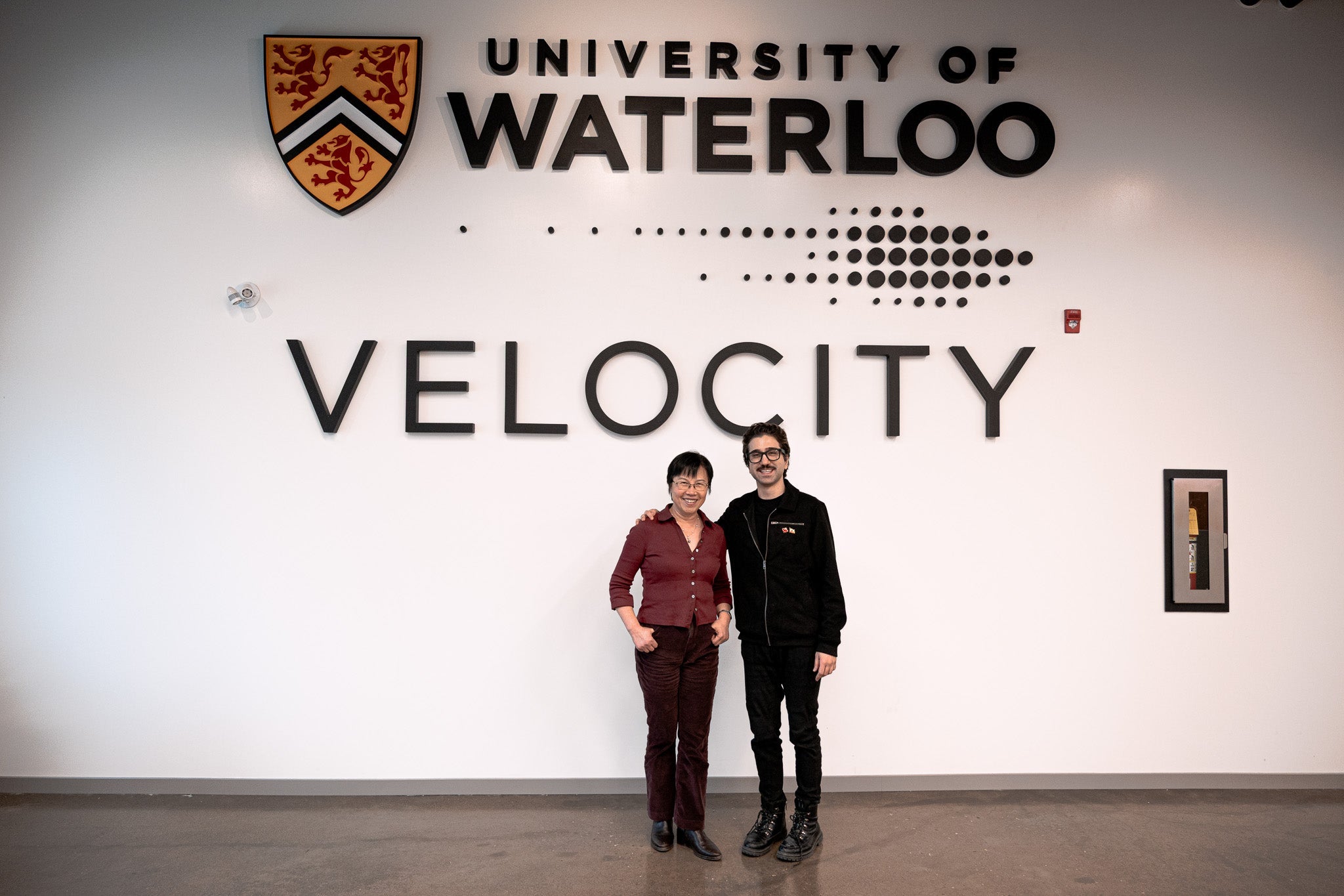 Dr. Helen Chen and Rastin Rassoli posing in front of the Velocity and University of Waterloo signage inside the Innovation Arena
