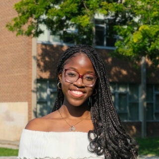 A young woman smiles in front of her school