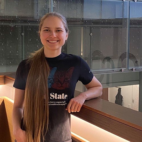 Emilia Dyrenkova leaning on a wooden railing inside IQC