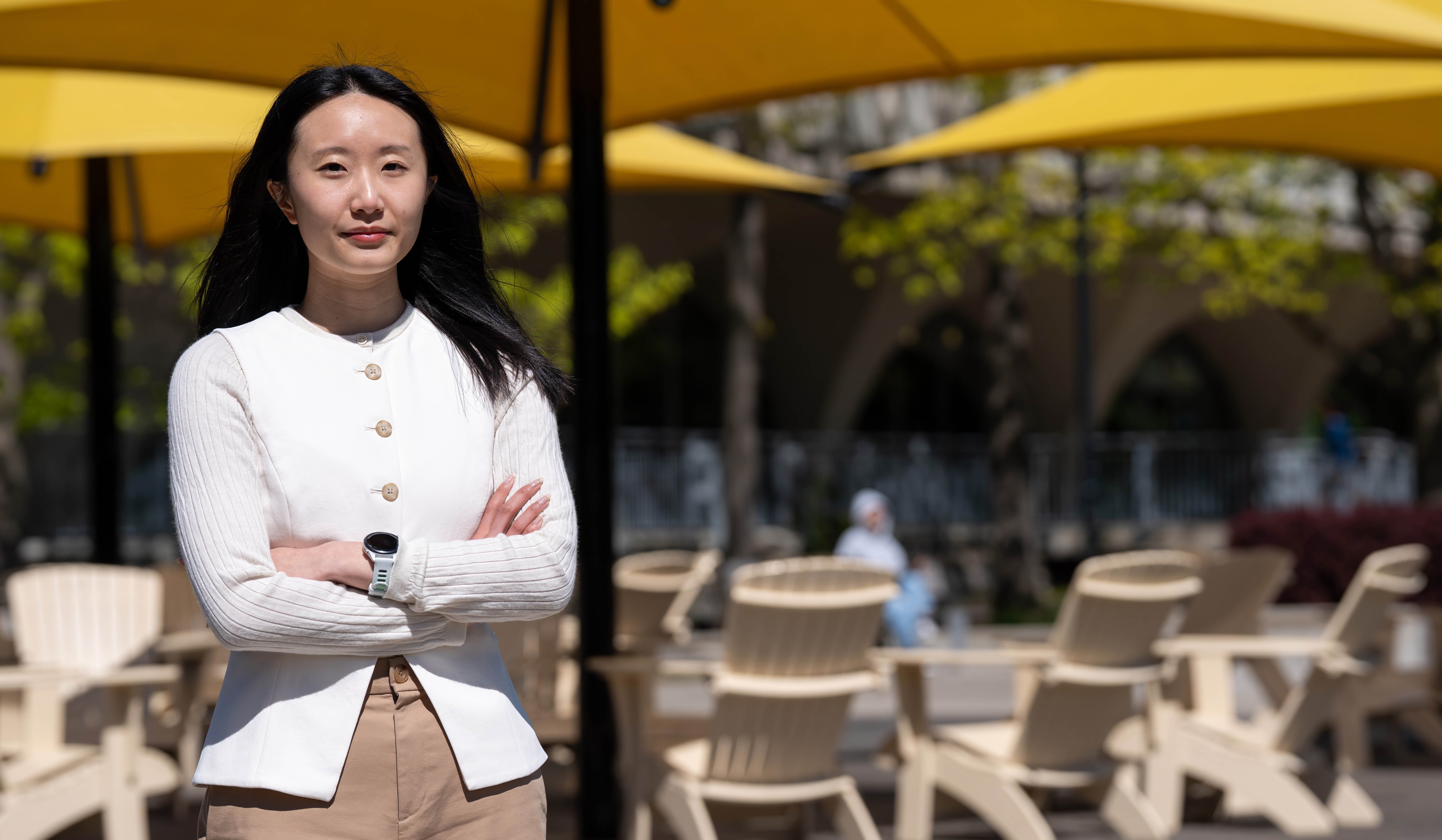 Yuki Yeung faces camera with arms crossed standing in front of large sun umbrella