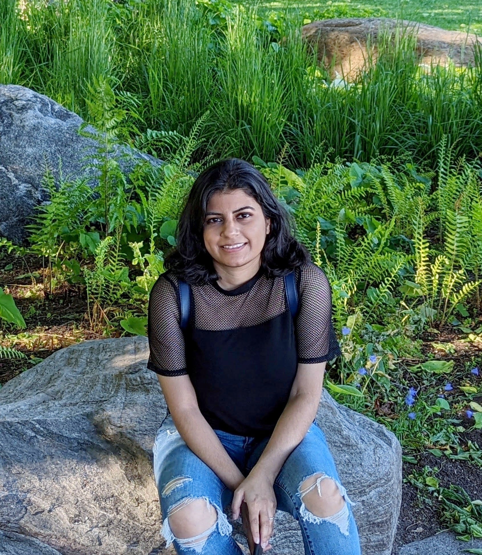 Aparajita sitting on a large rock in a garden