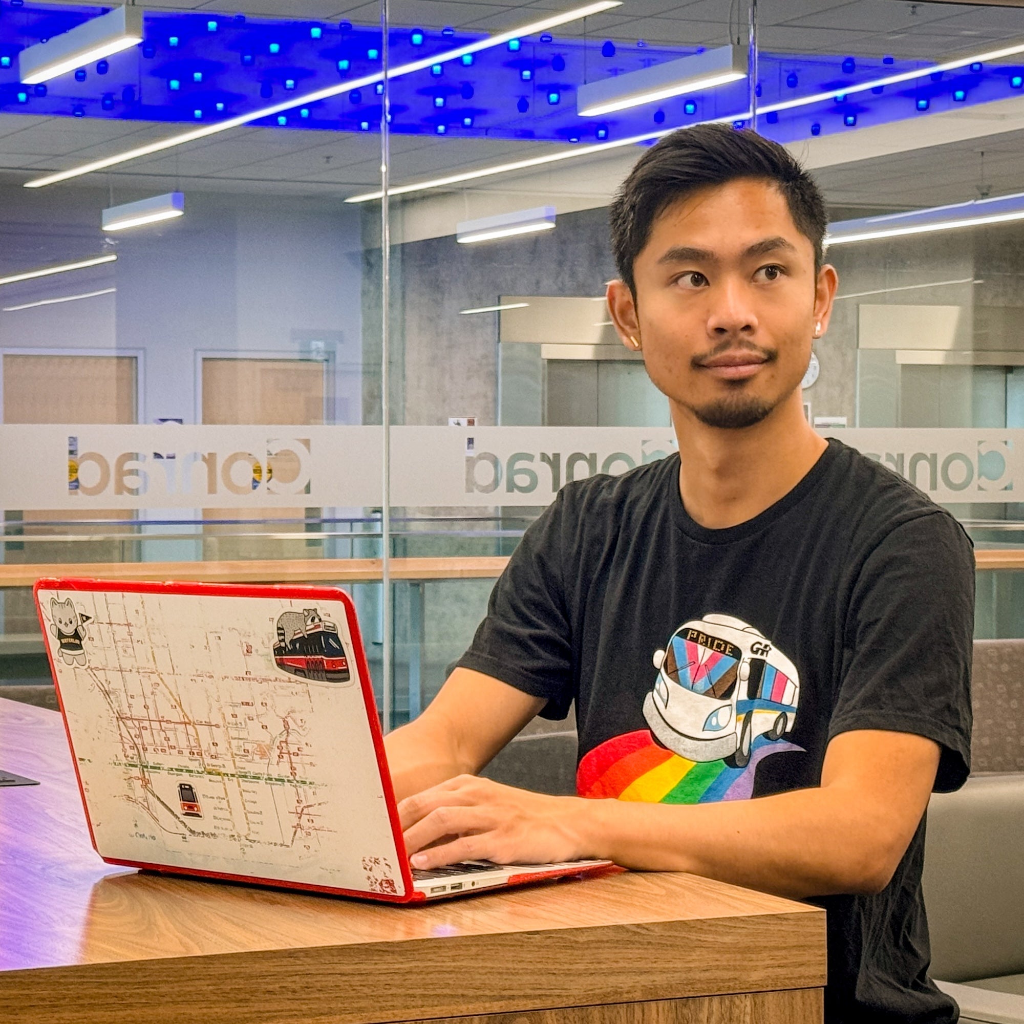 Rodney Chan wearing Grand River Transit's pride t-shirt and working on his laptop