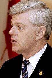 Side of John Manley's face as he stands in front of a Canadian flag