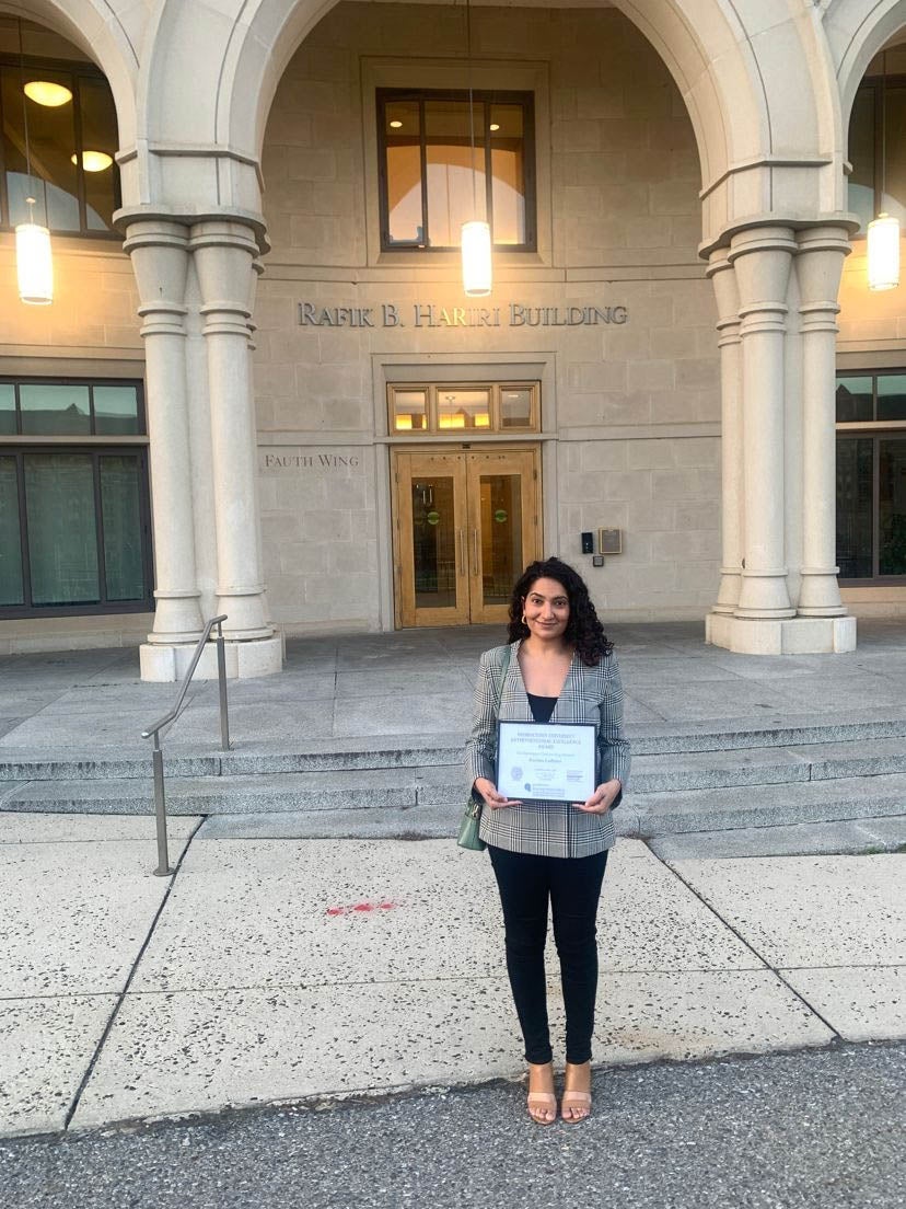 Person stands outside entrance of a building holding a framed diploma