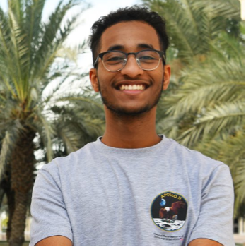 Mohamed Yousuf wearing a grey t-shirt and dark framed glasses, smiling at the camera