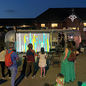 People standing outside a bus watching a piece of art on a projected screen