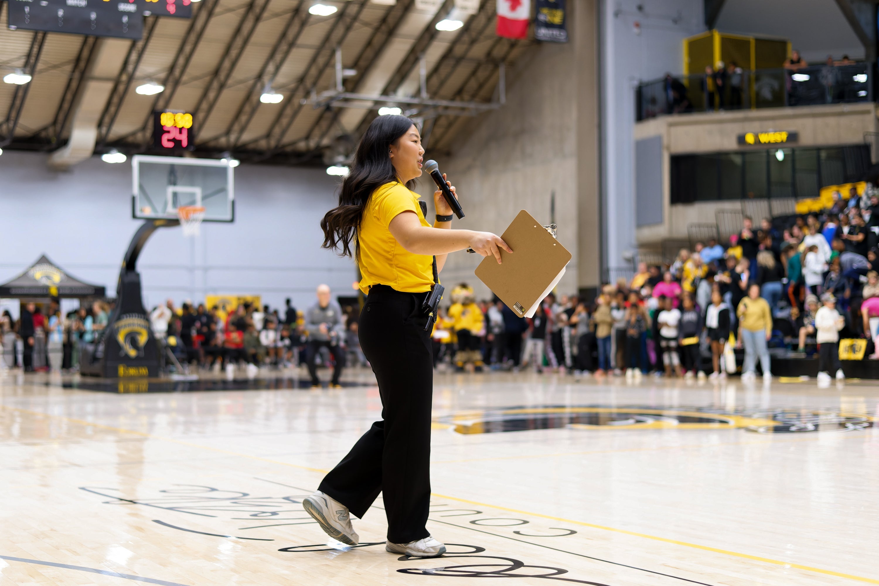 Diane Choi dressed in Warriors support gear speaks into microphone while presenting to crowd in a large gym