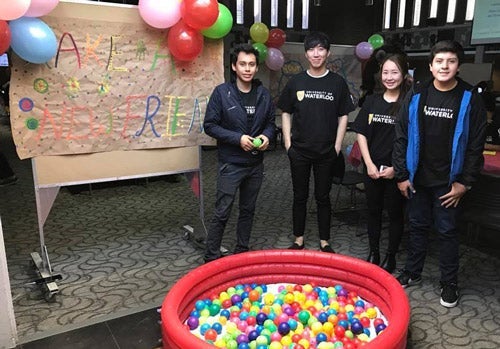 Four waterloo students stand in front of kindness kiddie pool and sign that reads "Make a new friend"