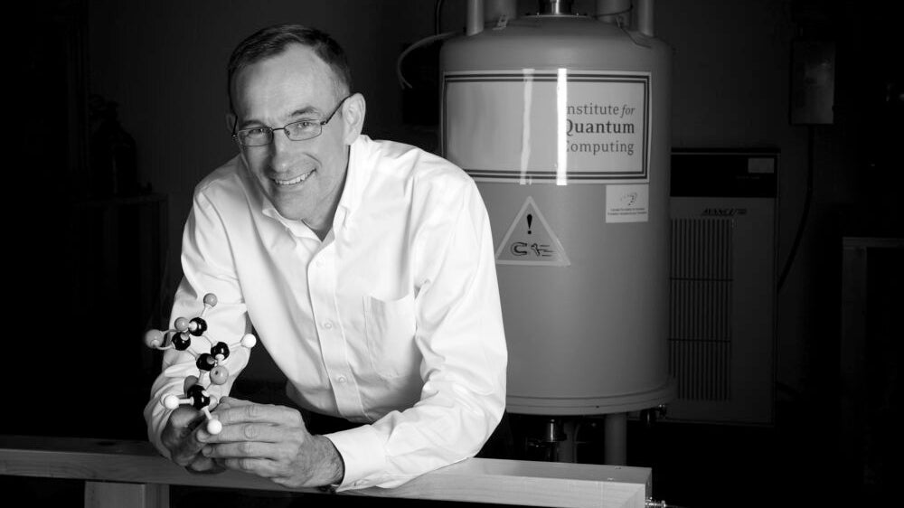 Raymond LaFlamme in a lab holding a molecular model