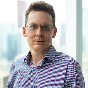 Richard Wintle wearing a plaid blue and white shirt with dark framed glasses