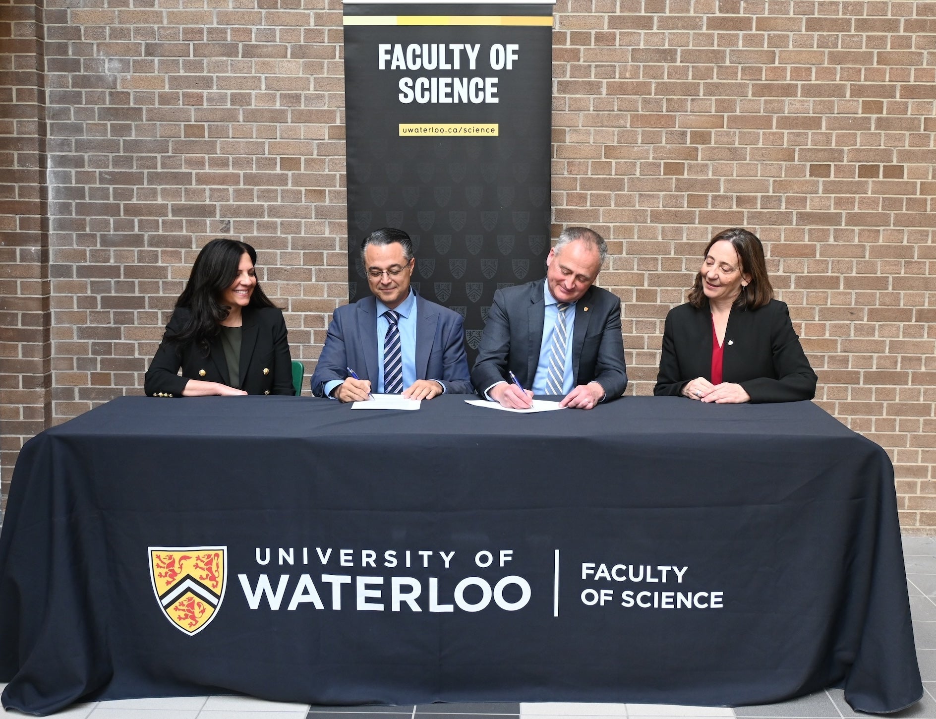 Two women and two men seated at a table signing a partnership agreement