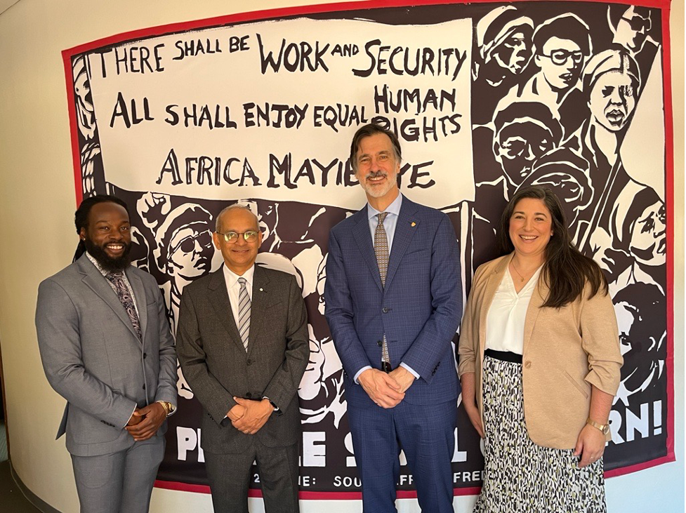 Four people in front of a mural that reads "There shall be work and security. All shall enjoy equal human rights."