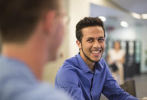 Man sitting in a campus building, laughing with a friend.