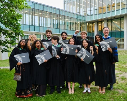 Groyp of SFM gradates in their conovcation robes holding diplomas and celebrating 