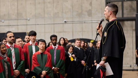 Lead Marshall speaks to graduates ahead of ceremony using microphone and standing on a riser