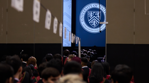 Graduates file into convocation ceremony. Large UWaterloo logo displayed on backdrop.