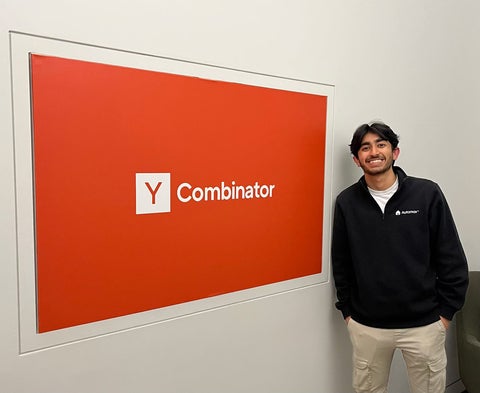 Humza Ahmed poses beside Y Combinator sign