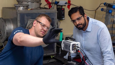 Graduate student Braden Southern and Dr. Vinny Gupta look at a battery cell while standing in front of experimental enclsure.