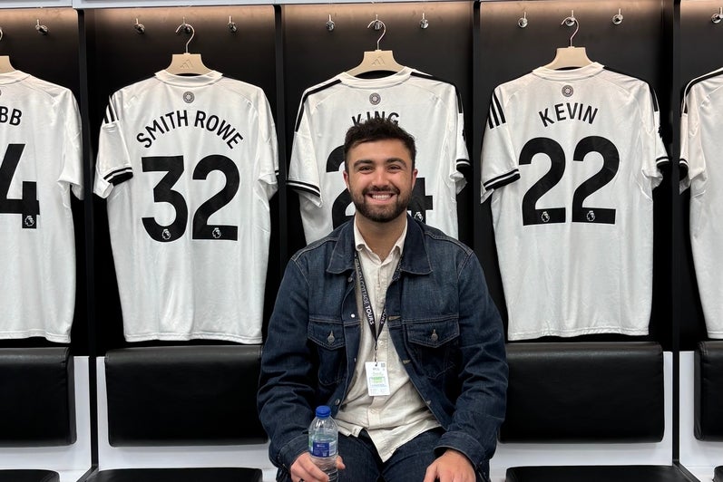 Ethan Rad sitting in a locker room with jerseys hanging on the wall behind him