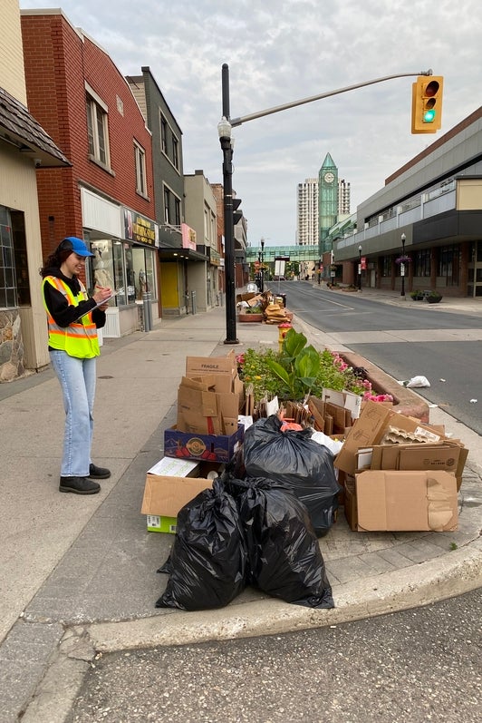 Chloe Sullivan in protective gear, writing down on a notepad about waste collection found on the side of street