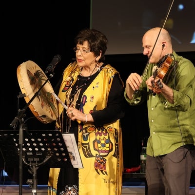 Shannon Thunderbird, Coast Tsm’syen singer-songwriter, and Chris McKhool, the Sultans of String leader, performing on stage.