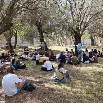 School of Architecture cohort in Rome sitting on the ground of a park, sketching on notepads while listening to Rick Haldenby talk 
