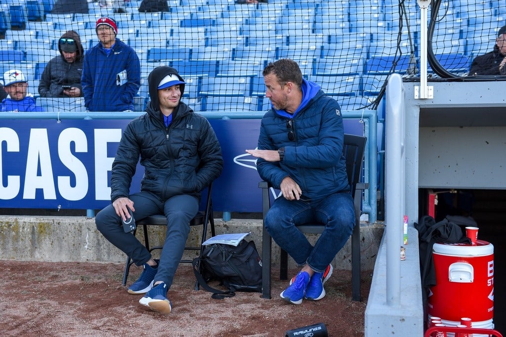 Jesse Levine chats with TJ Burton while seated beside a baseball dugout.