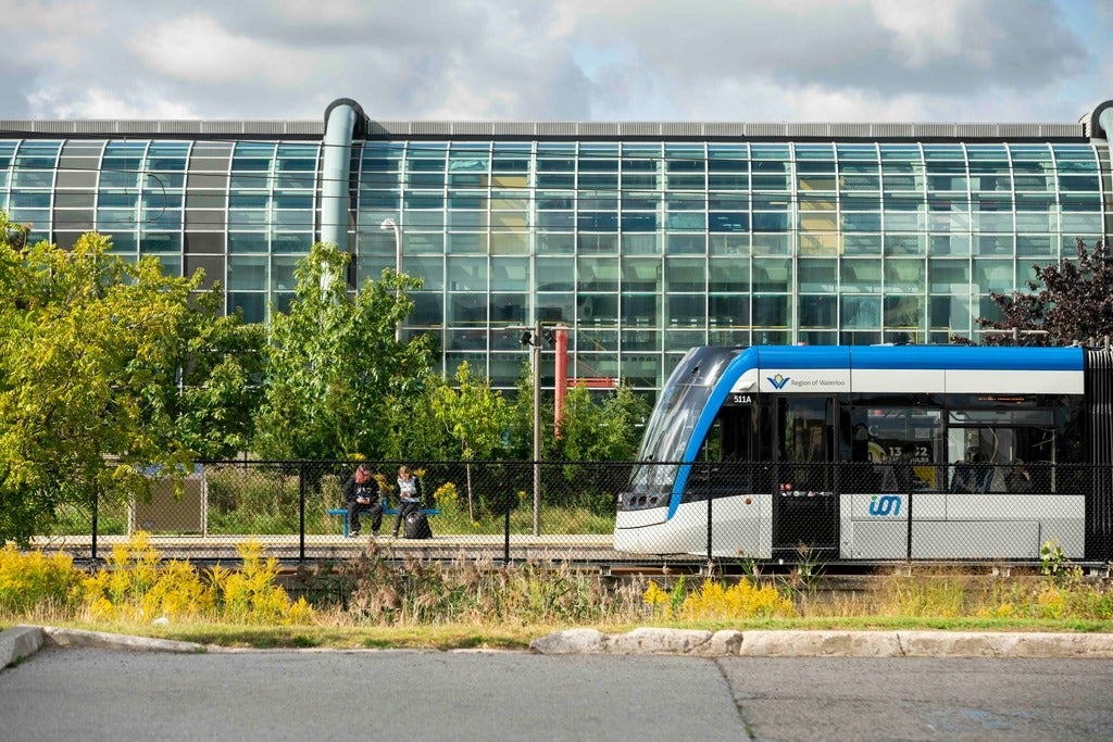 Train passes two people seated on a bench in front of the Davis Centre