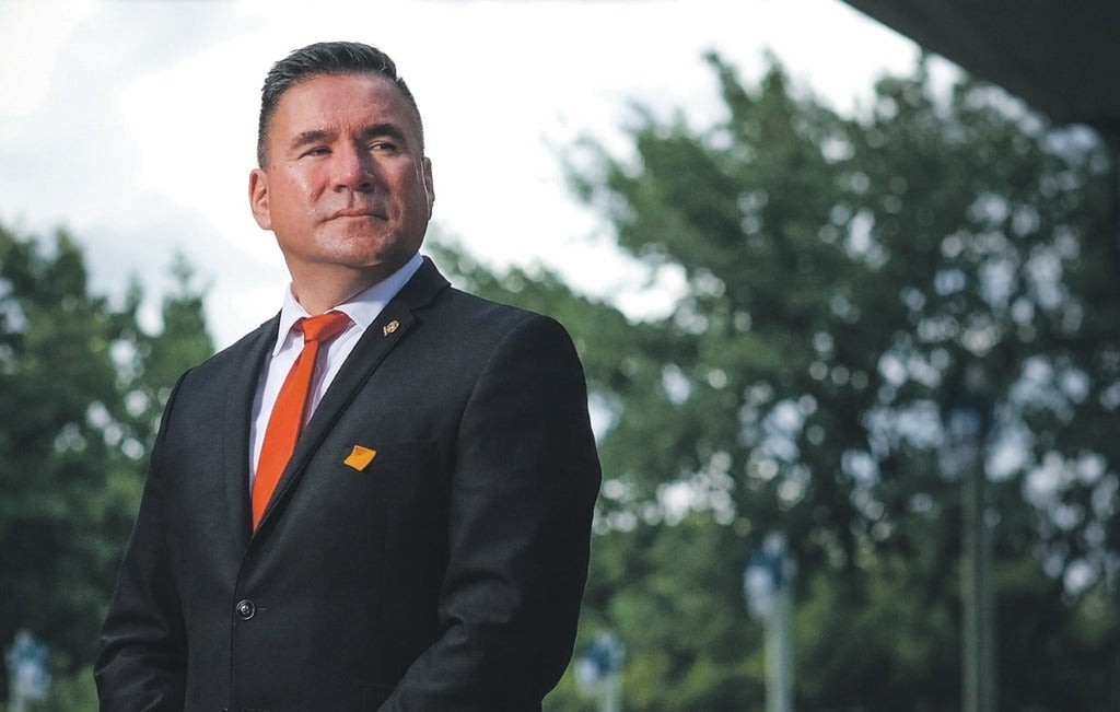 Brad Regehr standing outside in front of trees. He's wearing a suit with an orange tie and pin