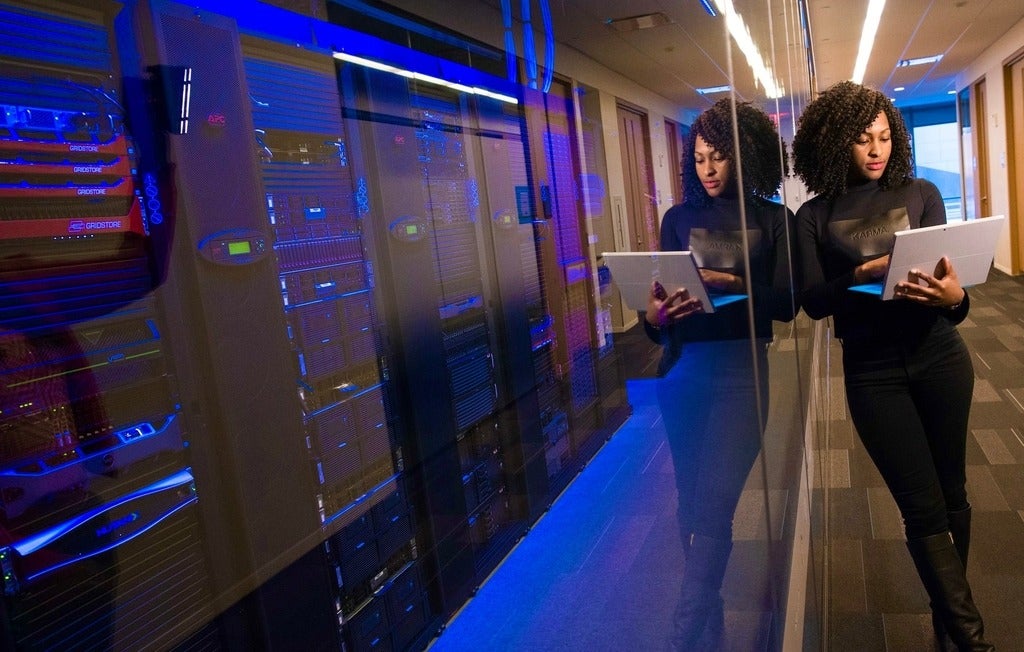 Black woman with laptop beside large computers