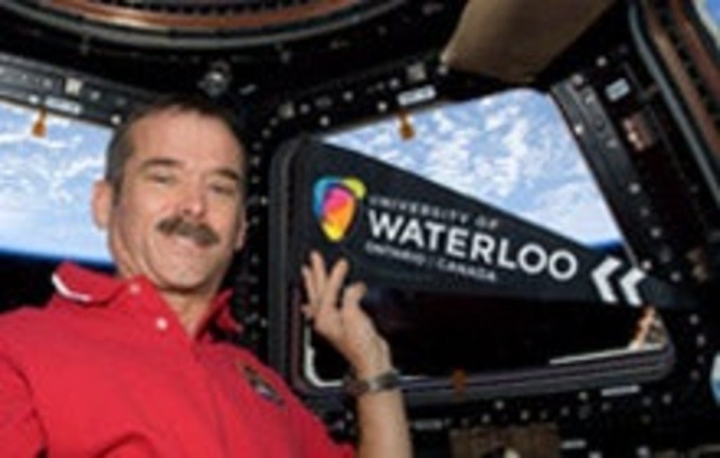 Chris Hadfield holding University of Waterloo pennant in space