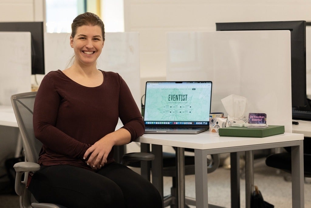 Ciara Azam sitting by a desk with a laptop showing the Eventist landing page next to a box of tissues and trinkets