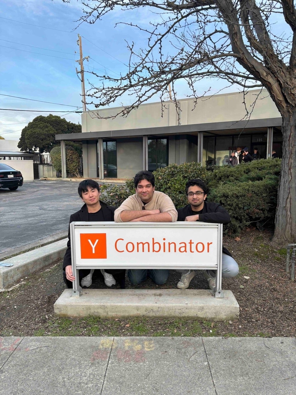 Three Waterloo students stooping behind "Y Combinator" sign