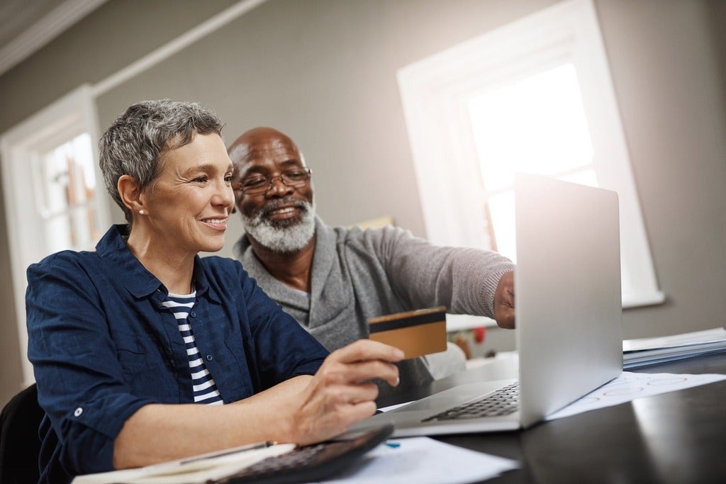 A senior couple using a credit card and laptop while working on their finances at home.
