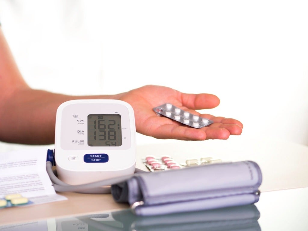 Person measuring their blood pressure with a sphygmomanometer while holding blood pressure pills
