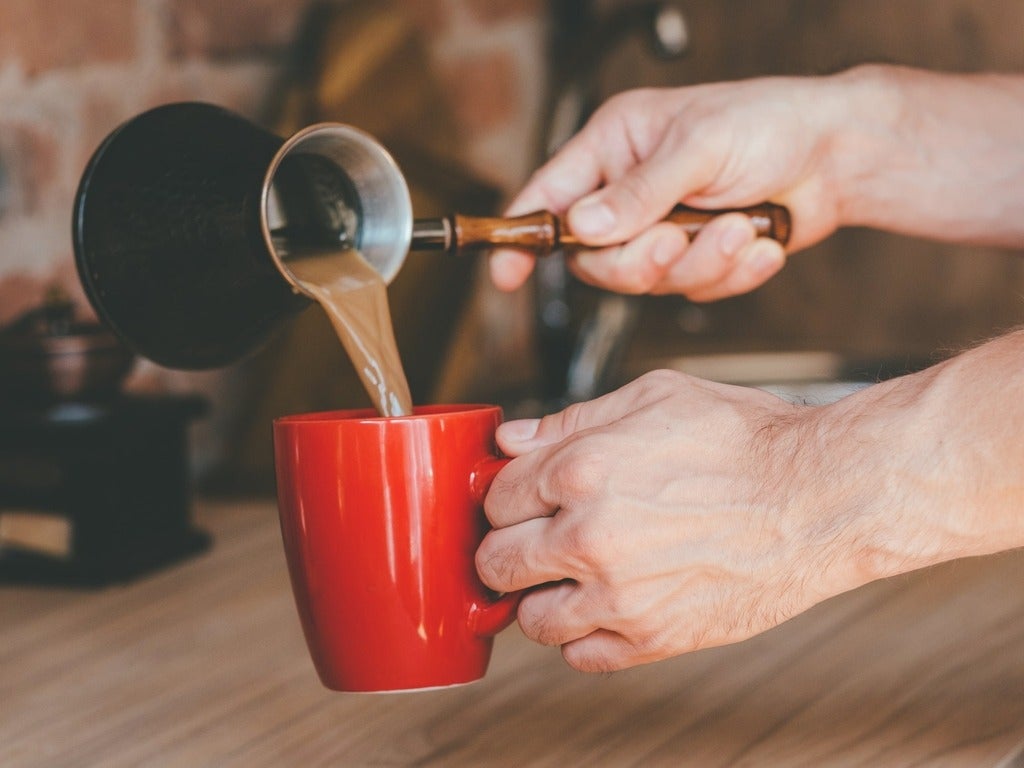 Man with jezve pouring latte into red mug.