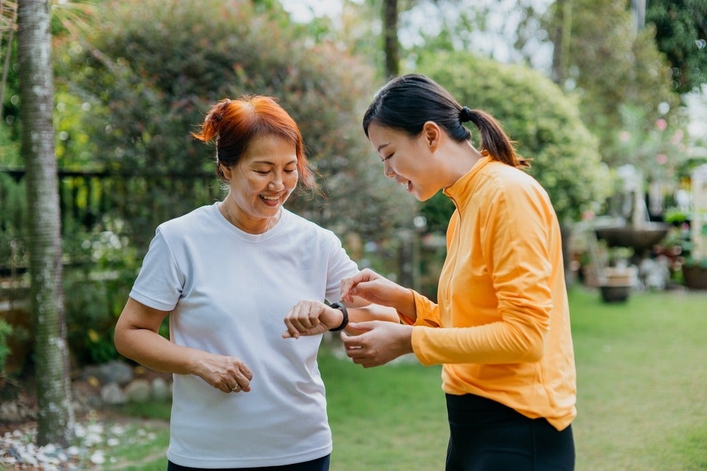 An Asian woman looks at a fitness tracker on her mother's wrist 