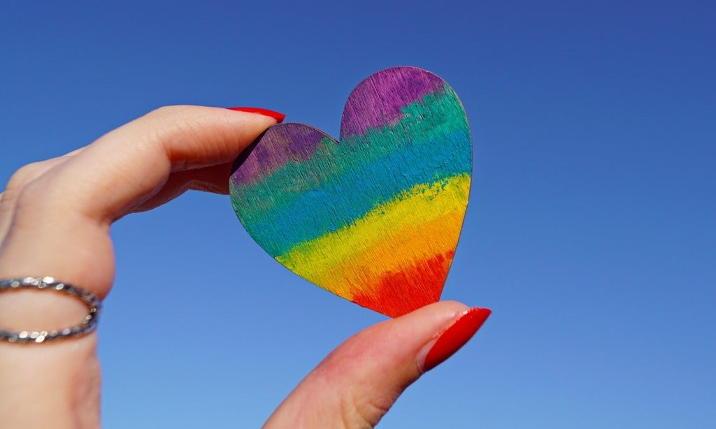 hand holding heart shaped wood peice with rainbow colours
