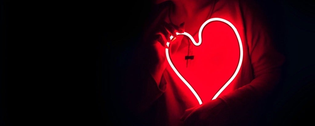Glowing outline red outline of heart in the dark being held up by two hands