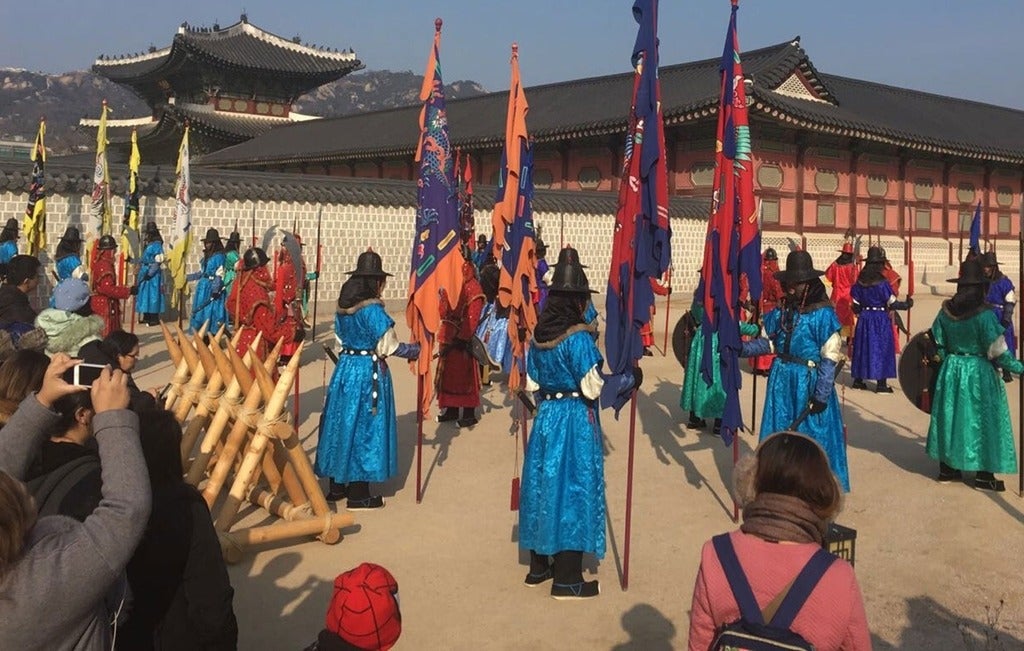 A photo taken in South Korea of people standing in bright coloured robe holding large flags.