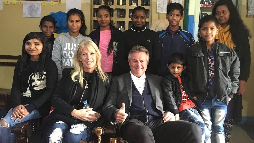 Stacey Cootes and Michaels Steele sit on a couch surrounded by Indian elementary school students