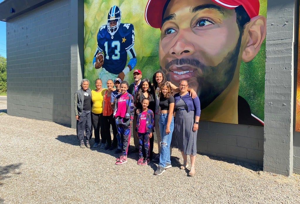 Taly Williams poses with family members in front of a new mural of him on the wall of the arena in Haliburton.