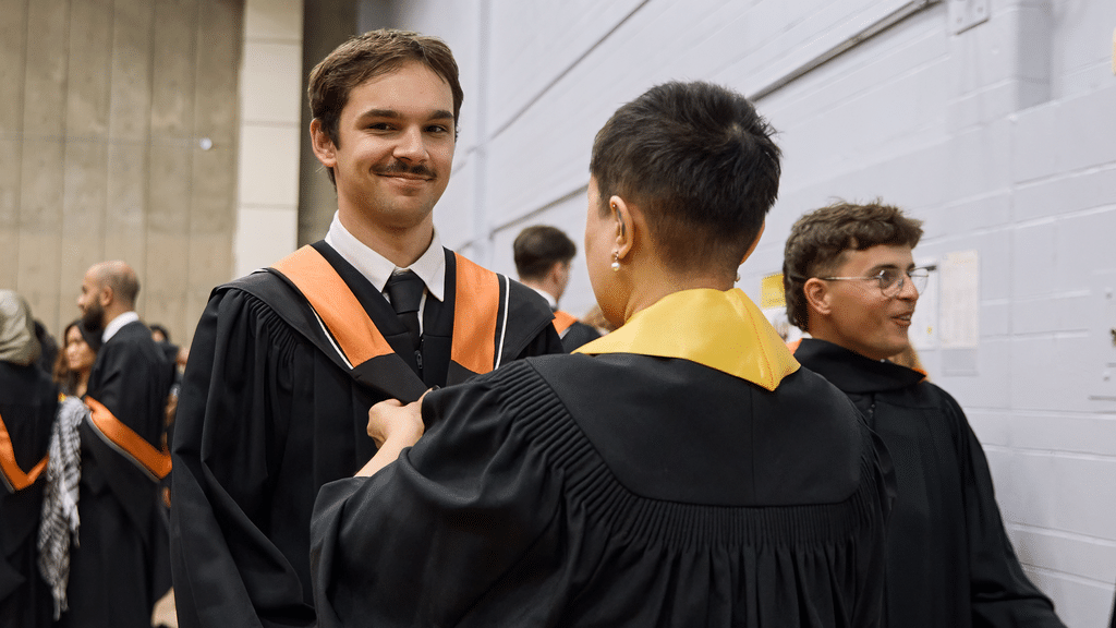 Graduate smiles at camera while marshall helps them hood
